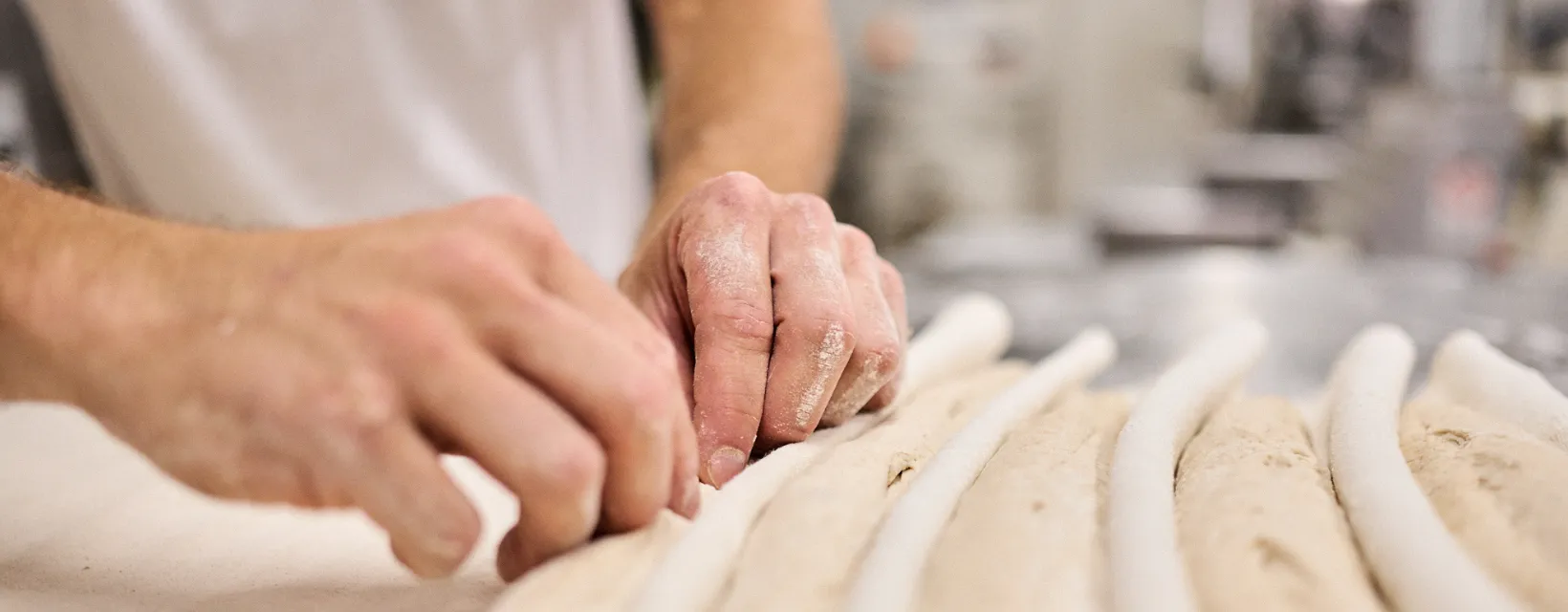 Le mani di un panettiere che formano i filoni sul banco infarinato